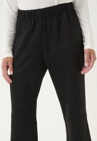 Pantalones de ante negro con una cinturilla elástica, con una textura suave y un diseño de pierna recta. Primer plano del detalle del tejido.