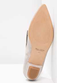 Zool van een lichtgrijze suède schoen met een spitse neus, een gestructureerde beige zool en de tekst "Marc O'Polo Made in Portugal 4½" zichtbaar.