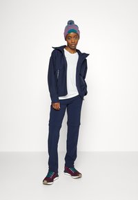 Veste d'extérieur bleu marine avec un pantalon assorti, un t-shirt blanc en dessous, et un bonnet en tricot coloré avec un pompon. Équipé de baskets.