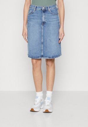 Jeansrock in Hellblau, knielang mit leichter A-Linien-Form, Fünf-Taschen-Design und sichtbaren Nähten entlang des Saums. Kombiniert mit weißen Sneakern.