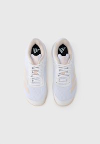 Zapatillas deportivas blancas con parte superior de malla, acentos crema y suelas de color claro; cuentan con tres rayas beige en cada lado.