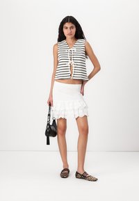 Haut sans manches à motifs noir et blanc avec fermeture à nouer, associé à une jupe blanche en dentelle volantée et des ballerines à imprimé léopard. Sac à main noir inclus.