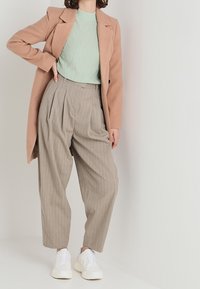 Ljusrosa lång kappa över en grovstickad mintgrön tröja, kombinerat med högmidjade, beige randiga byxor och vita sneakers.