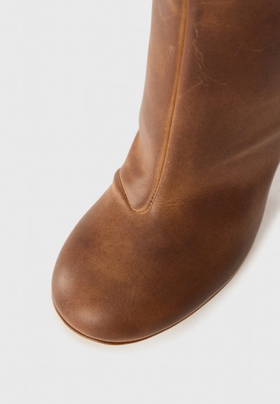 Brown leather ankle boot with a rounded toe, smooth texture, and subtle stitching detail along the seam. Simple and minimalist design.