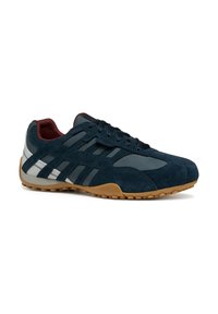 Scarpa sportiva in suede blu navy con dettagli grigi e strisce riflettenti. Presenta una suola in gomma e una superficie testurizzata. Design con lacci.