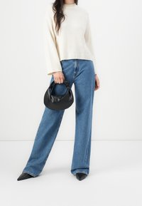 Jasnobeżowy sweter o szerokich rękawach, połączony z wysokim stanem i luźnymi niebieskimi dżinsami. Czarna, usztywniana torebka i czarne szpilki w szpic.