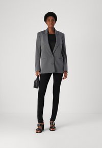 Gray oversized blazer with two buttons, worn over a black top. Paired with black skinny pants and chunky-heeled sandals with buckles.
