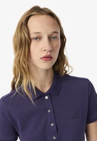 Polo shirt viola realizzato in tessuto testurizzato, con colletto e placket a cinque bottoni; presenta un piccolo logo ricamato sul petto.