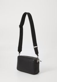 Black rectangular crossbody bag in synthetic material, featuring a zip closure, silver hardware, and an adjustable black strap with logo detail.