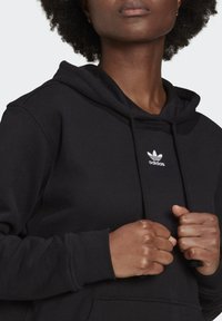 Svart hoodies med huva i bomullsblandning, med en vit Adidas-logotyp på bröstet, texturerat tyg och justerbara snörningar.