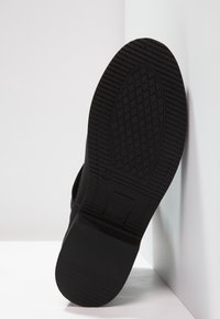 Suela de zapato negra con una superficie texturizada que presenta un patrón de diamante; incluye un corte rectangular y un detalle de tamaño en relieve.