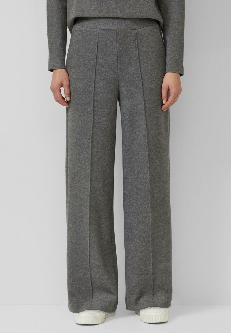 Szare spodnie o szerokich nogawkach wykonane z miękkiego materiału z plisami z przodu; posiadają gładki pas i zwężane zakończenie, zestawione z białymi trampkami.