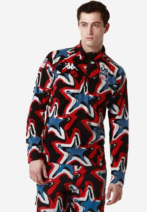 Pullover in pile con zip caratterizzato da un motivo vorticoso in rosso, nero, blu e bianco. Include un patch con la bandiera americana e il logo della squadra di sci.