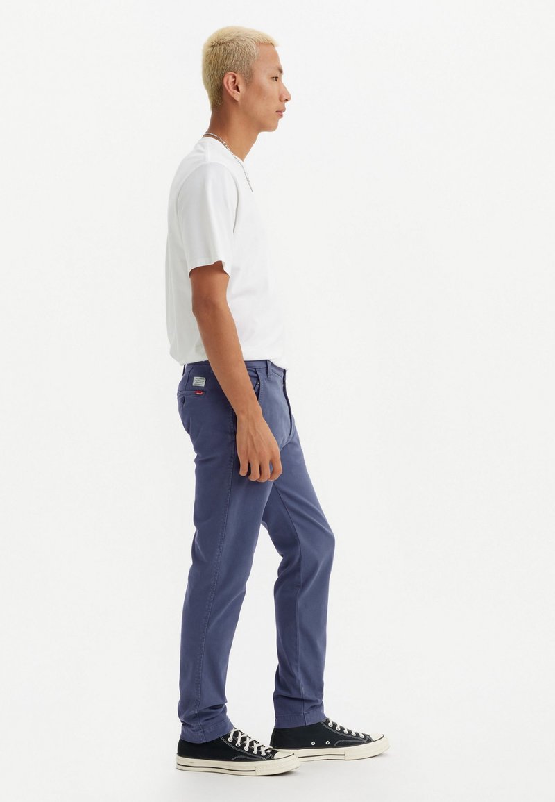 Pantalones azul marino en corte slim, hechos de algodón, con una textura suave y bolsillos en la parte frontal, combinados con una camiseta blanca de manga corta y lisa.