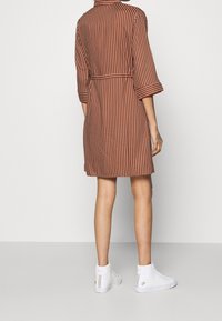 Robe rayée marron et blanche avec des manches trois-quarts, une ceinture à la taille et une coupe décontractée, associée à des baskets montantes blanches.