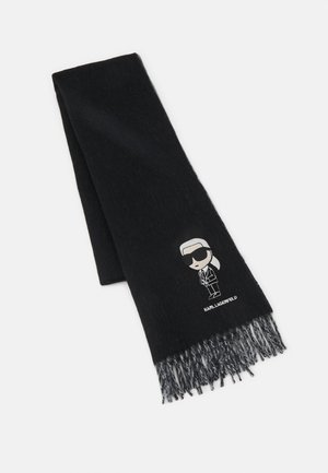 Écharpe noire avec franges aux extrémités et petite figurine de dessin animé portant des lunettes de soleil et un costume près du logo indiquant KARLLAGERFELD.
