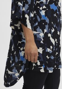 Blommig blus i mörkblått, vitt och ljusblått. Flödande tyg, vida ärmar och rundad nederkant. Bärs med svarta leggings.