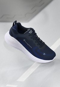 Navy athletic shoe with a smooth upper, textured detailing, white sole, and prominent logo. Features laces and a rear pull tab for easy wear.