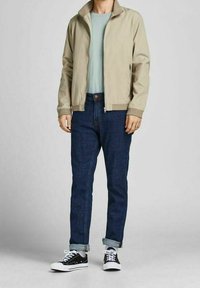 Béžová lehká bunda, modré tričko, tmavě modré džíny, černo-bílé tenisky. Bunda má zip a žebrované manžety. Jednoduchý design.