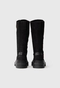 Stivali alti in suede neri con suola piatta in gomma, caratterizzati da una texture liscia e dettagli di cucitura verticale, progettati per una silhouette aderente.