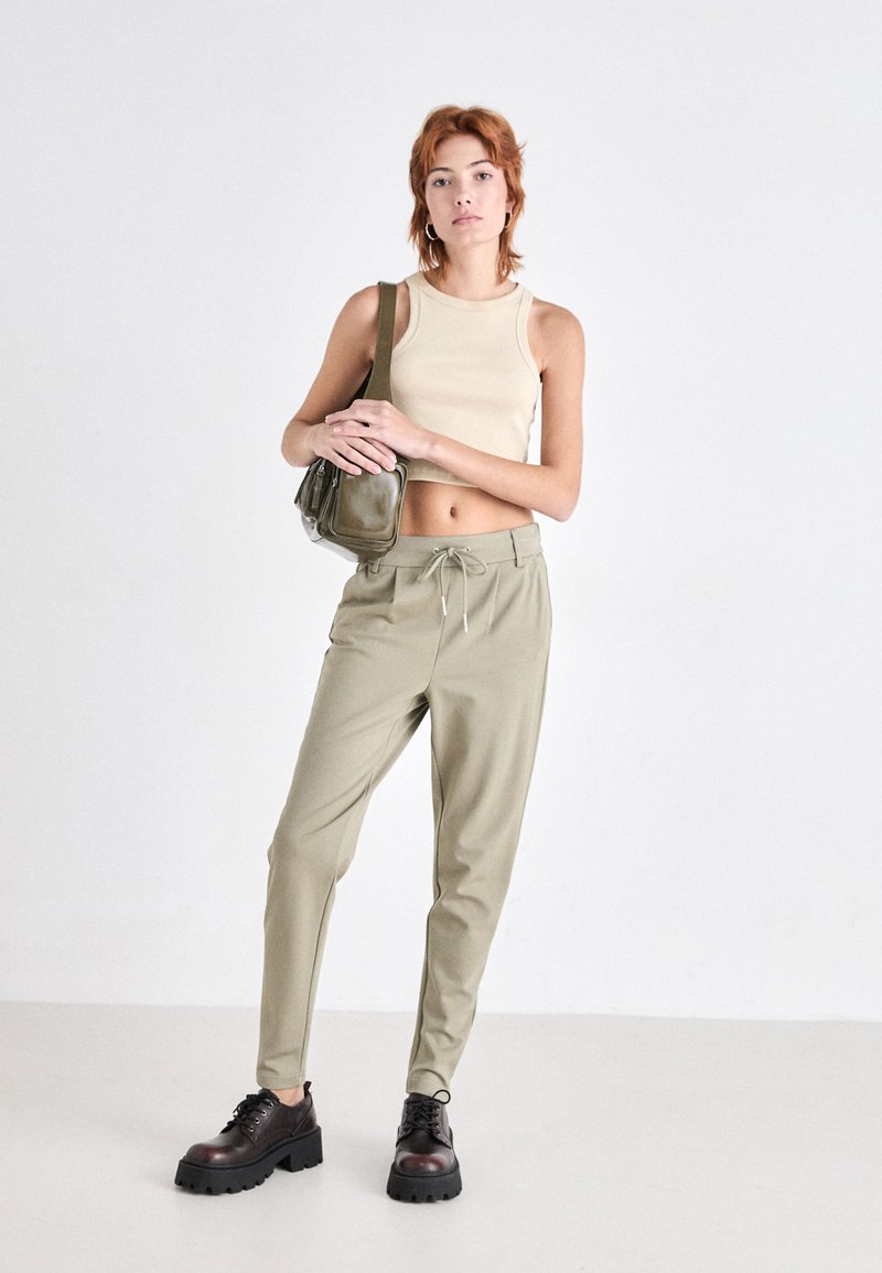 Beige Cropped-Top, olivgrüne Hose mit elastischem Bund und schwarze Plateauschnürschuhe. Minimalistisches Design und lockere Passform.