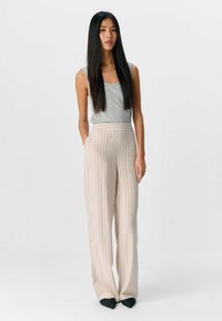 Lichtgrijze tanktop gecombineerd met beige pantalon met pinstripes en wijde pijpen. De broek heeft een hoge taille en zakken, de stof heeft een gladde textuur.