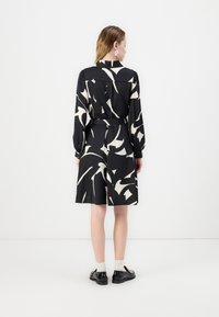 Black dress with white abstract pattern, long sleeves, belted waist, knee-length skirt, paired with black shoes and white socks.