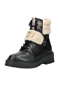 Zwarte leren enkellaars met dikke zool, beige schapenvachtmanchet en riem, gouden logohardware en zwarte veter op witte achtergrond.