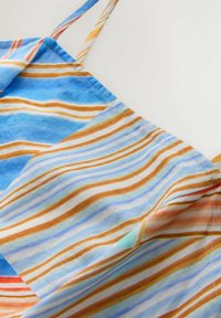 Blåt og orange stribet stof med tynde stropper, der viser overlappende folder og synlige syningsdetaljer.