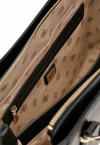 Intérieur de sac à main en matière synthétique noire avec une doublure beige, comportant une poche zippée, du matériel de marque et un motif subtil.