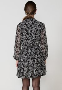 Rochie neagră cu flori, cu mâneci lungi din material transparent, talie ajustată și fustă evazată. Model floral alb pe toată suprafața țesăturii.