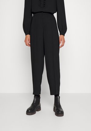 Pantaloni neri a vita alta con un design su misura, caratterizzati da due pieghe frontali, una texture liscia e una vestibilità ampia, abbinati a stivaletti neri.
