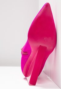 Talons aiguilles fuchsia avec un bout pointu et une texture satinée lisse. Elle présente un talon rose brillant et des détails de couture subtils.