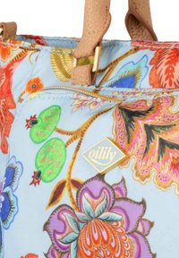 Kleurrijke stoffen tas met bloemenpatroon in blauw, met een gouden rits en een gouden logo-label. Accenten in rood, groen en paars met gestructureerde handvatten.