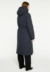 Lång marinfärgad pufferjacka med huva, insydd midja, elastiska mudd och en slät, isolerad yta. Designad för värme och funktionalitet.