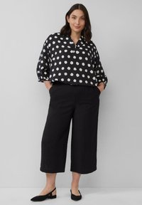 Schwarz-weiß gepunktete Bluse mit Kragen, lockerer Passform und 3/4 Ärmeln, kombiniert mit lockeren schwarzen Crop-Hosen und schwarzen Ballerinas.