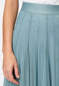 Light blue, pleated skirt made of sheer fabric. Features a wide waistband and layered texture for depth and movement.