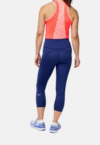 Débardeur de sport ajusté en corail vif avec un dos à motifs, associé à des leggings navy de longueur genou présentant des détails de couture et un logo.