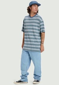 Ριγέ κοντομάνικο t-shirt σε μπλε αποχρώσεις, με στρογγυλή λαιμόκοψη και άνετη εφαρμογή. Φοριέται με ανοιχτόχρωμα φαρδιά τζιν και μαύρα sneakers.