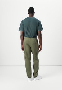 Green cotton t-shirt and olive cargo pants with side pockets, featuring an elastic waistband. White sneakers complete the outfit.