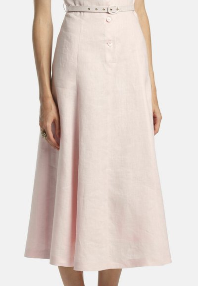 Žena v svetloružovej midi sukni áčkového strihu s opaskom a gombíkovým detailom vpredu, na jednoduchom pozadí.