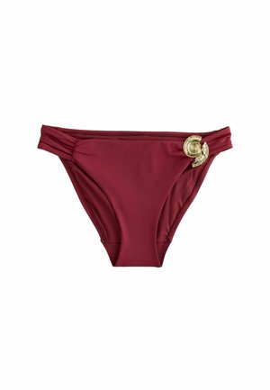 Bordowe majtki od bikini z marszczonymi bokami i ozdobną złotą muszlą na prawej biodrze.