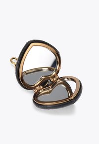 Lusterko w kształcie serca z czarną skórzaną powłoką i złotym metalowym wykończeniem, z dwoma refleksyjnymi powierzchniami wewnątrz.
