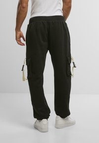 Svarte joggebukser med elastisk midje, sidelommer og beige stropper. Laget av mykt materiale med en glatt tekstur.