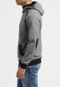 Sudadera gris con un diseño de punto texturizado, acentos negros en los hombros y puños, bolsillo canguro, estilo ajustado, hecha de una tela suave.