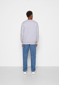 Felpa grigia chiara con collo a giro e polsini a coste, abbinata a jeans baggy blu in denim con tasche laterali e sneakers bianche.