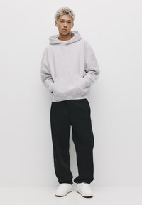 Szara, oversize bluza z kapturem i kieszenią kangurką, czarne luźne spodnie oraz białe sneakersy. Prosty design, miękka tekstura i neutralna paleta kolorów.
