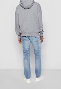 Sudadera con capucha gris de corte holgado, combinada con jeans de denim azul claro. Incluye detalles como costuras y un pequeño logotipo en el bolsillo trasero.