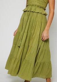 Green tiered maxi dress with a textured, lightweight fabric, featuring ruffles at the waist and gold flecks. Includes a drawstring with a tassel.