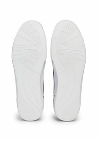 Suela de zapatillas blancas con un patrón de agarre texturizado, que presenta un logo circular y marcas a lo largo de la base para tracción y estabilidad.